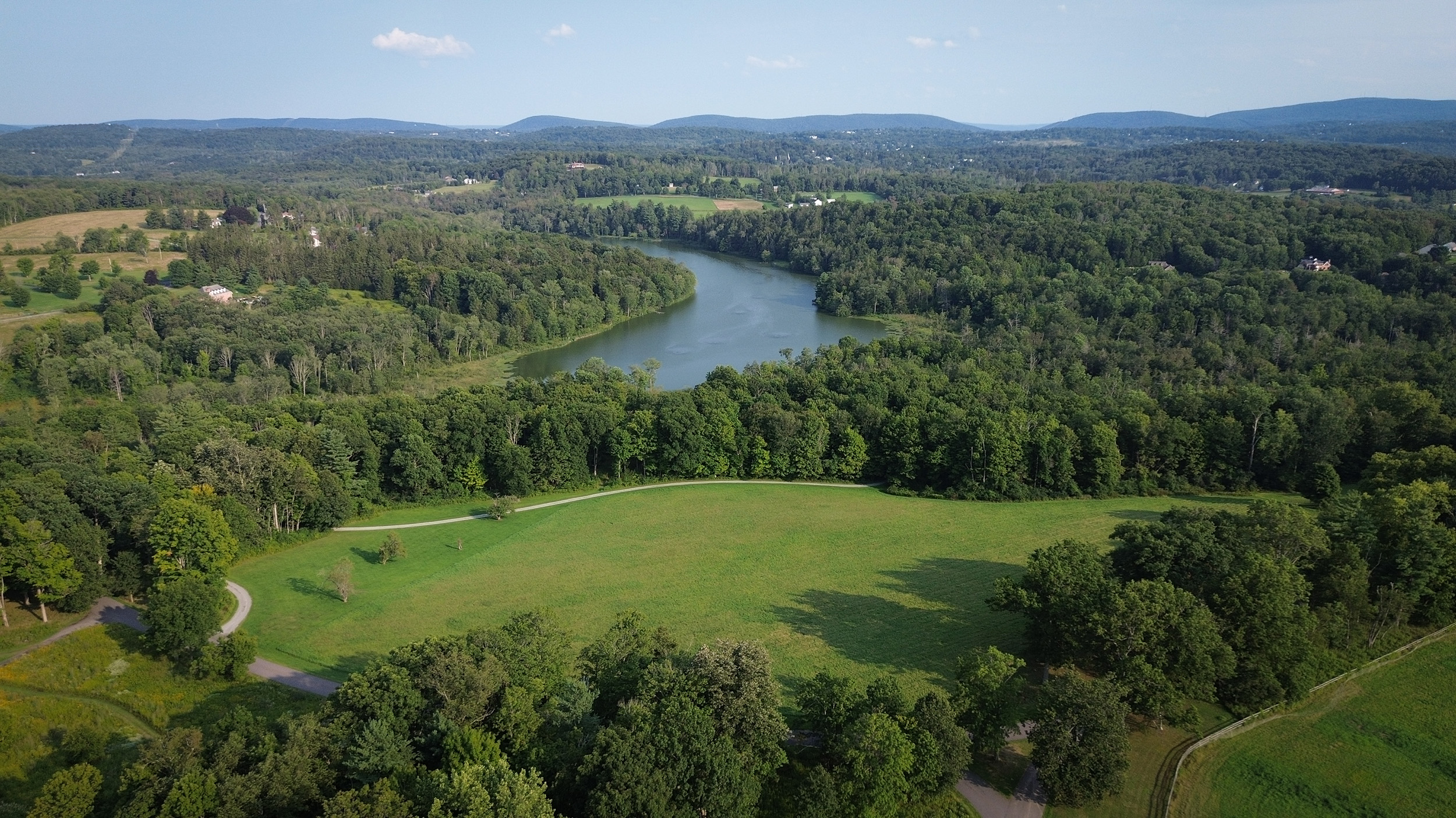 An aerial view of a field with forests and a river in the background.